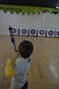 Child aiming bow at archery targets indoors