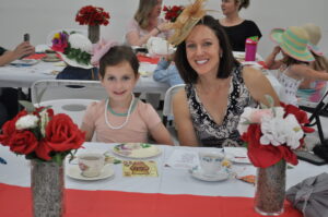 Women and children at tea party, wearing hats.